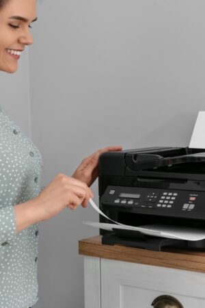 Woman,Using,Modern,Printer,On,Chest,Of,Drawers,At,Home