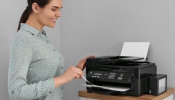 Woman,Using,Modern,Printer,On,Chest,Of,Drawers,At,Home